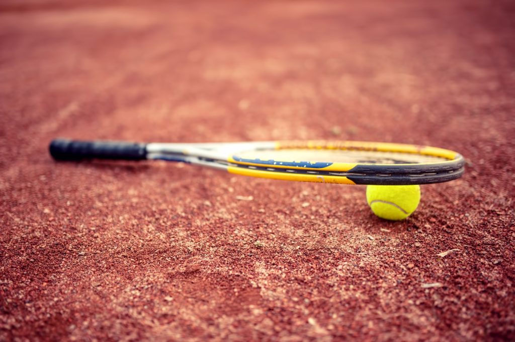 Close-up of tennis racket and ball on clay tennis court