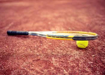 Close-up of tennis racket and ball on clay tennis court