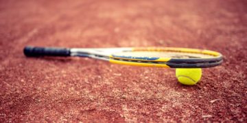 Close-up of tennis racket and ball on clay tennis court