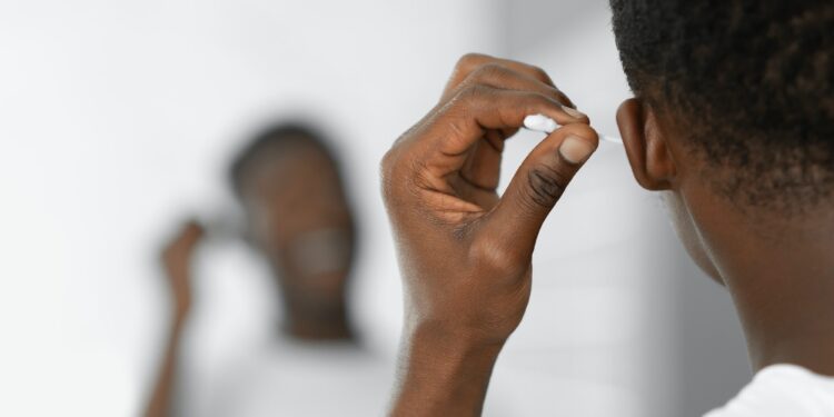 Black Man Cleaning Ears Using Cotton Swab Standing In Bathroom
