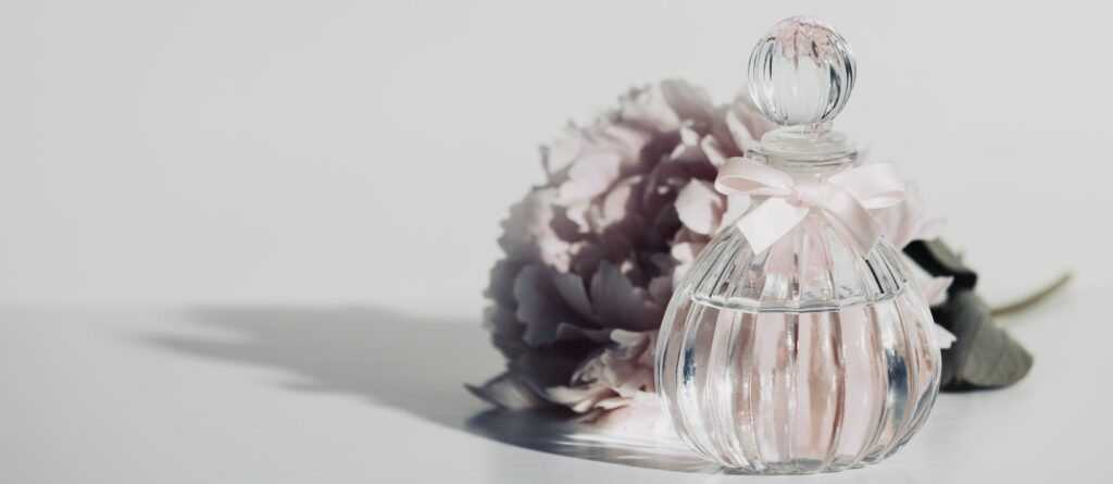 Pink peopy flower and perfume bottle against white wall, copy space