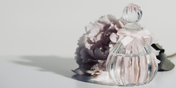 Pink peopy flower and perfume bottle against white wall, copy space